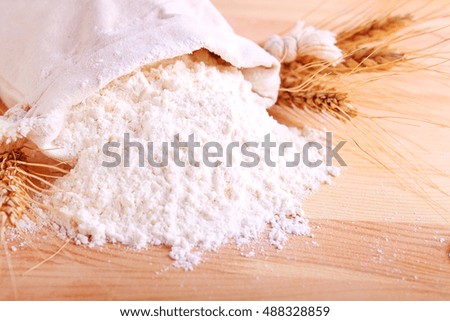 Baking ingredients: flour and ears on a light wooden background