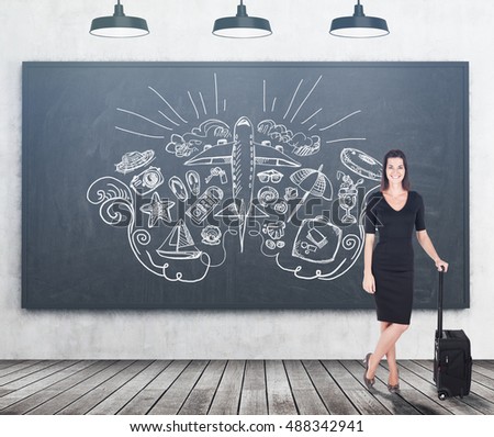 Smiling businesswoman in black is standing near chalkboard with giant plane and travelling sketches. Concept of tourism