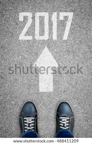 Black casual shoes standing on the asphalt concrete road and white direction sign telling to go straight to new year 2017