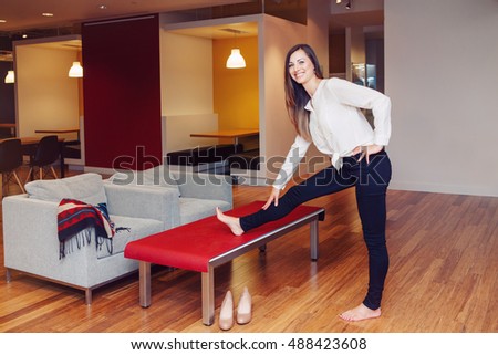 Portrait of slim fit sporty young white Caucasian business woman with long blond hair in white shirt meditating doing yoga exercisers on office table at work, healthy lifestyle concept.