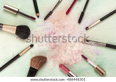 Makeup brushes and lipstick on teal blue background, with traces of powder and blush, forming a frame. Horizontal template for makeup artist's business card or flyer design, with copyspace