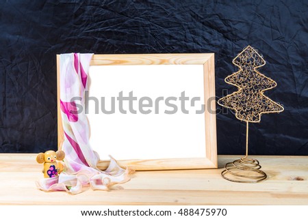 Christmas. Wooden empty picture frame with a white background is on the table. On the frame is scarf. Christmas tree decoration. Wooden toy. Dark blue background.