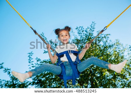 Girl in a city park on a trampoline jumping high on a background of trees and sky