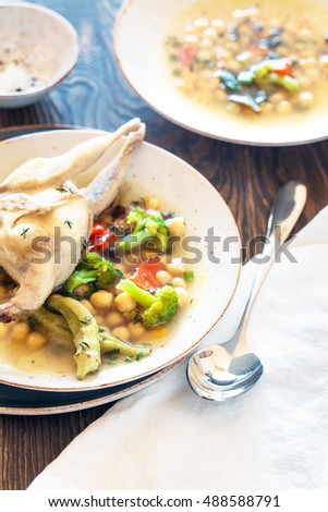 Soup with quail, broccoli, chick-pea and okra served in rustic plates on wooden table, close up view