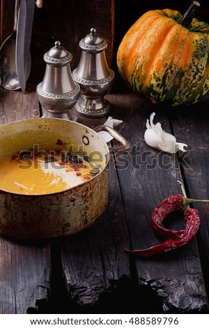 Spicy pumpkin cream soup served in the vintage metal pan with cream and chili flakes on rustic wooden background