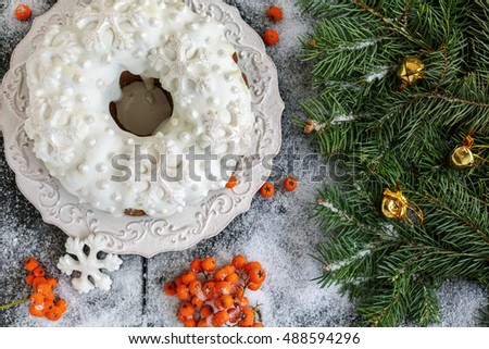 Christmas cake, mountain ash and spruce branches on a snowy wooden background.