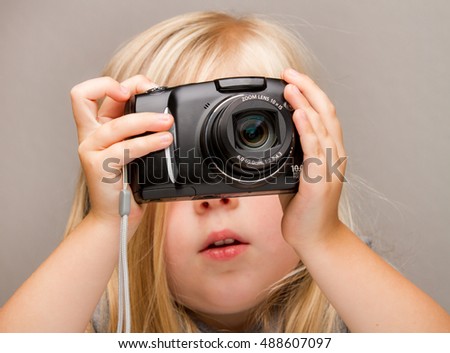 Young child holding a point and shoot camera. Focus is on the camera as she is about to push the button