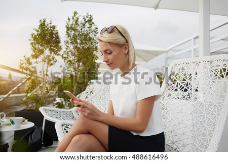Female CEO is searching information in internet via cell telephone, while is sitting on hotel balcony. Young hipster girl is chatting in social network via mobile phone, while is relaxing in cafe