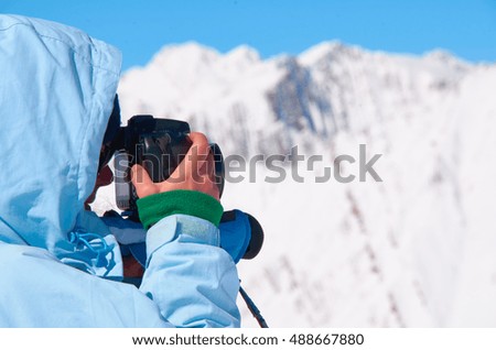 Girl in blue jacket with photo camera in mountains take a picture of snow peaks. Relax or recreation concept.