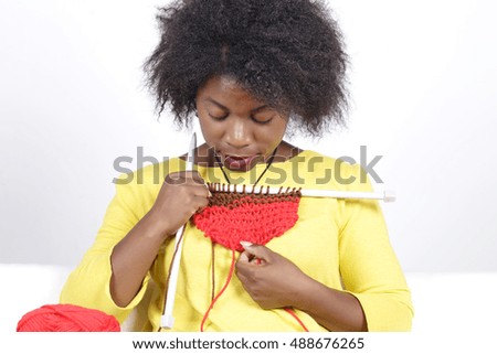 African woman knitting, sitting on a white couch. Mixing brown with red colour.
