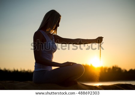 Beautiful girl pours sand from his hands on the sunset background