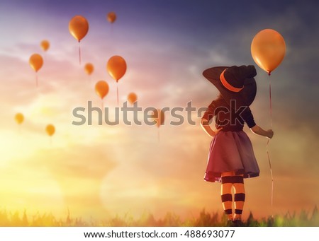 Happy Halloween! Cute little witch with a air ball. Beautiful young child girl in witch costume outdoors. 