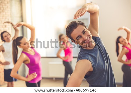 Beautiful sports people are stretching and smiling while doing yoga in modern fitness hall