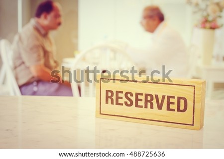 reserved sign made from wooden plate in restaurant with blurred image of people.