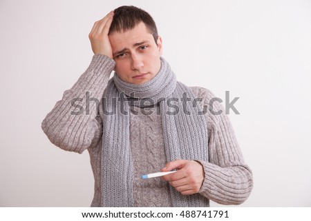 Unhealthy young man holding a thermometer, neutral background