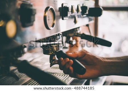 Barista holds a portafilter making coffee with a coffee machine. Toned picture