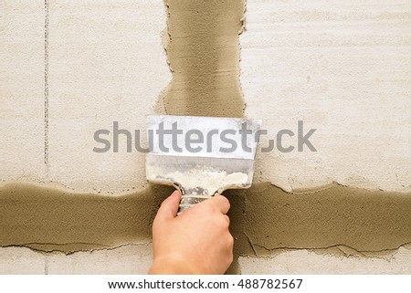 Man repairs wall with spackling paste, Construction industry worker using a putty knife and leveling concrete on concrete pillars, Worker spreading plaster to wall, corner protecting batten install