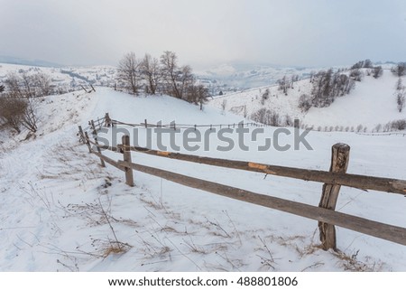 Rural alpine winter landscape with fence and path, serene blue sky
