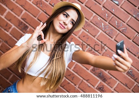 Beautiful stylish girl making selfie on brick wall background