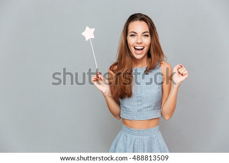 Happy amazed young woman holding magic wand over grey background