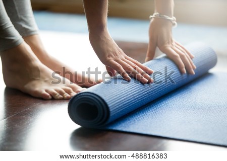 Close-up of attractive young woman folding blue yoga or fitness mat after working out at home in living room. Healthy life, keep fit concepts. Horizontal shot Royalty-Free Stock Photo #488816383