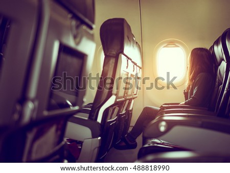 Lady is sitting in airplane looking out at shiny sun through window, vintage style photo Royalty-Free Stock Photo #488818990