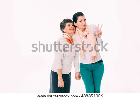 Smiling young female showing victory sign is standing close to senior mother - isolated on white