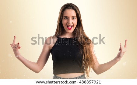 Young girl making horn gesture over ocher background