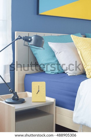 Yellow modern clock on bedside table with colorful pillows in background