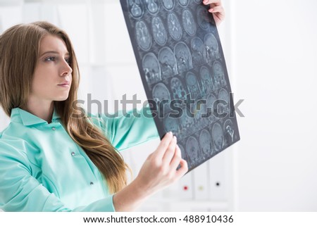 Beautiful woman doctor in green gown is looking at x ray image. Concept of brain surgeon work