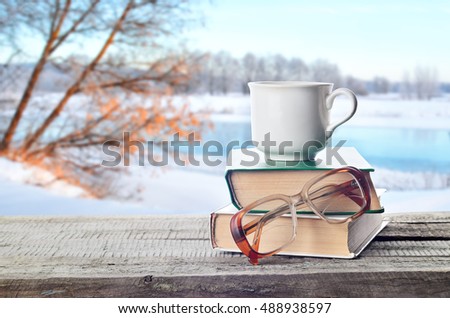 Hot coffee or tea, cocoa, chocolate cup on book and eyeglasses outdoors in winter. Pile of books, glasses and cup in nature.