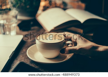 Young woman having a cup of coffee and reading a book in a cafe. Toned picture