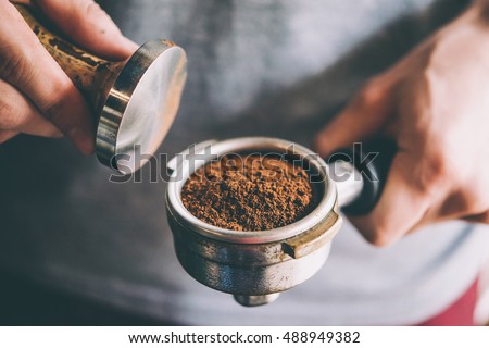 Barista presses ground coffee using tamper. Toned picture