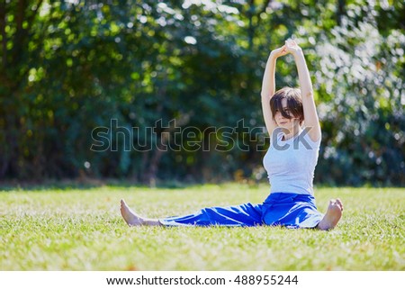 Young woman doing yoga outdoors in tranquil environment of green park on a summer sunny day. Serene relaxed female yoga instructor