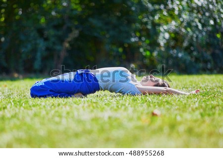 Young woman doing yoga outdoors in tranquil environment of green park on a summer sunny day. Serene relaxed female yoga instructor