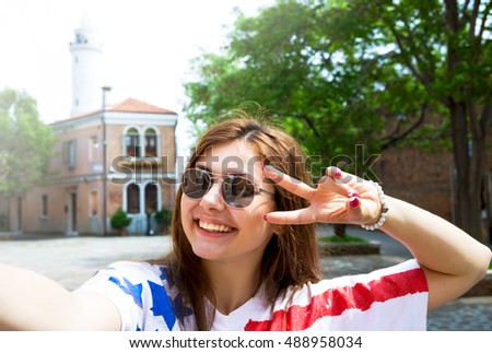 Summer lifestyle fashion portrait of young funny girl having fun, taking selfie in italy city , wearing trendy shirt with american flag print.Tourist lifestyle.Tourist woman taking mobile phone selfie