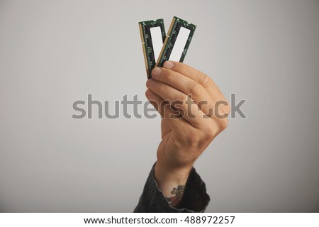 Close up of a tattooed man's hand with two RAM planks with chips against white wall background