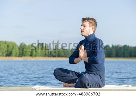 Man relaxing and practicing yoga on the lake footbridge early morning.