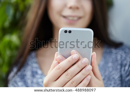 Girl using modern dual camera smartphone. Stereo cameras is the future of mobile technology. Smiling young model on the background. Buy new smart phone