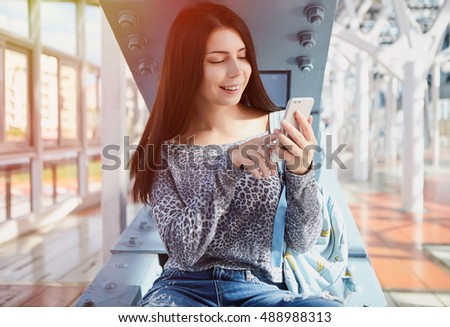 Pretty young girl use new big dual camera smart phone.Fashionable young woman and modern gadget.Most popular smartphone model with two cameras on back panel.Happy brunette girl use mobile application