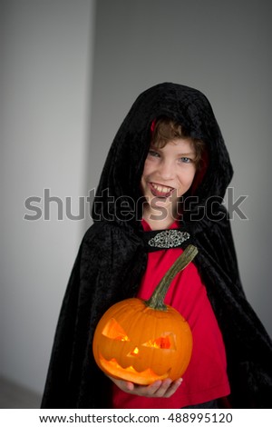 All Hallows Eve. Boy age dressed in a costume for Halloween. He represents the evil wizard. Boy is gowned in a black-red toga with a hood. He holds pumpkin with a candle inside - Jack o lantern