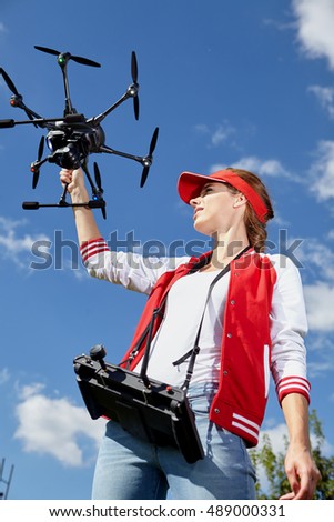 A woman is standing and holding drone over sky