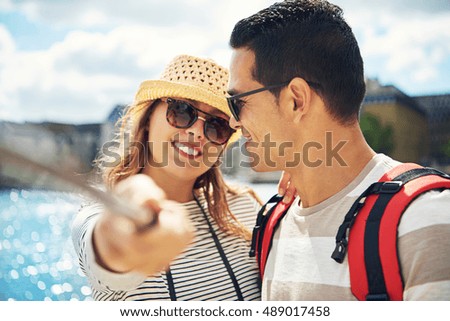 Happy attractive young woman in a trendy hat posing together with her husband for a selfie on their summer vacation at the coast