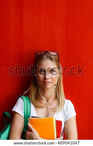 Young woman with headphones on background blank red Wall