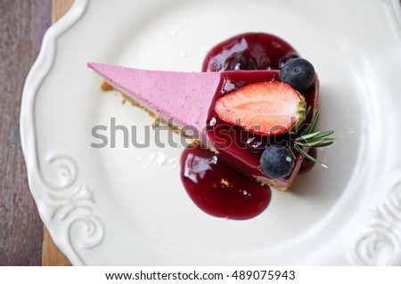 Top view of blueberry cheesecake with fresh strawberry on white plate.