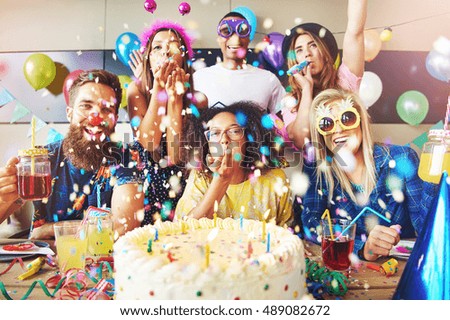 Confetti flying around group celebrating a party with large cake and drinks on table in front of them