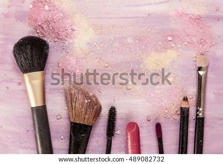 Makeup brushes, lipstick and pencil on a light purple background, with traces of powder and blush on it. A horizontal template for a makeup artist's business card or flyer design, with copyspace