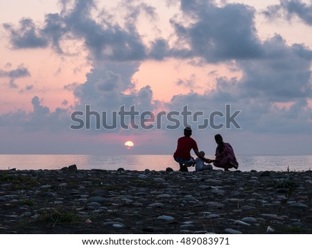 Happy family - father, mother, baby son see sunset sea surf on black sand beach. Active parents and people outdoor activity  tropical summer vacations with children.