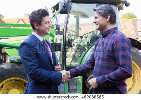 Farmer And Businessman Shaking Hands With Tractor In Background Royalty-Free Stock Photo #489088585