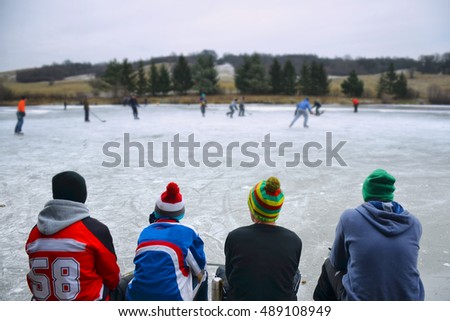 Young boys sitting on bench and looking at hockey game on natural ice. Scenery from rural sport event